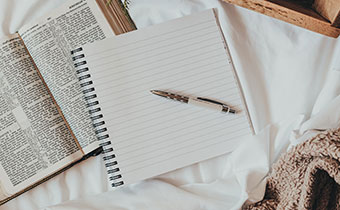 book and notepad on bed with coffee